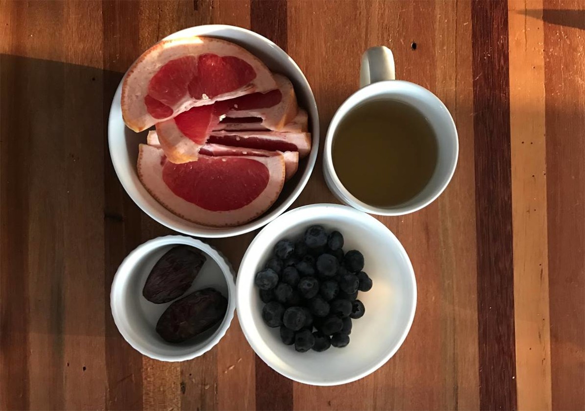 Breakfast featuring grapefruit, blueberries, and dates with green tea.